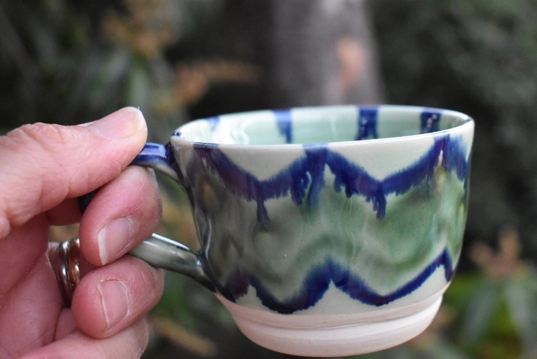 Hand holding a ceramic mug with blue and green glaze detailing on the sides